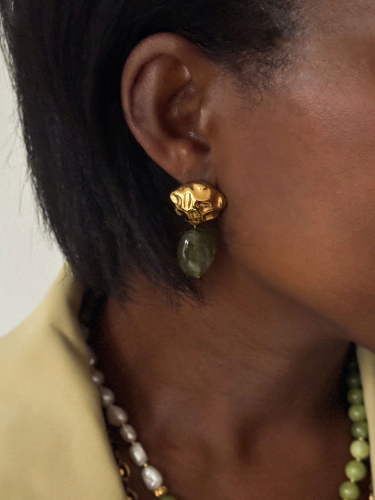 Close-up van een vrouw met gouden statement oorbellen met een donkergroene kraal uit de Atelier Colore collectie van Don’ aparte.