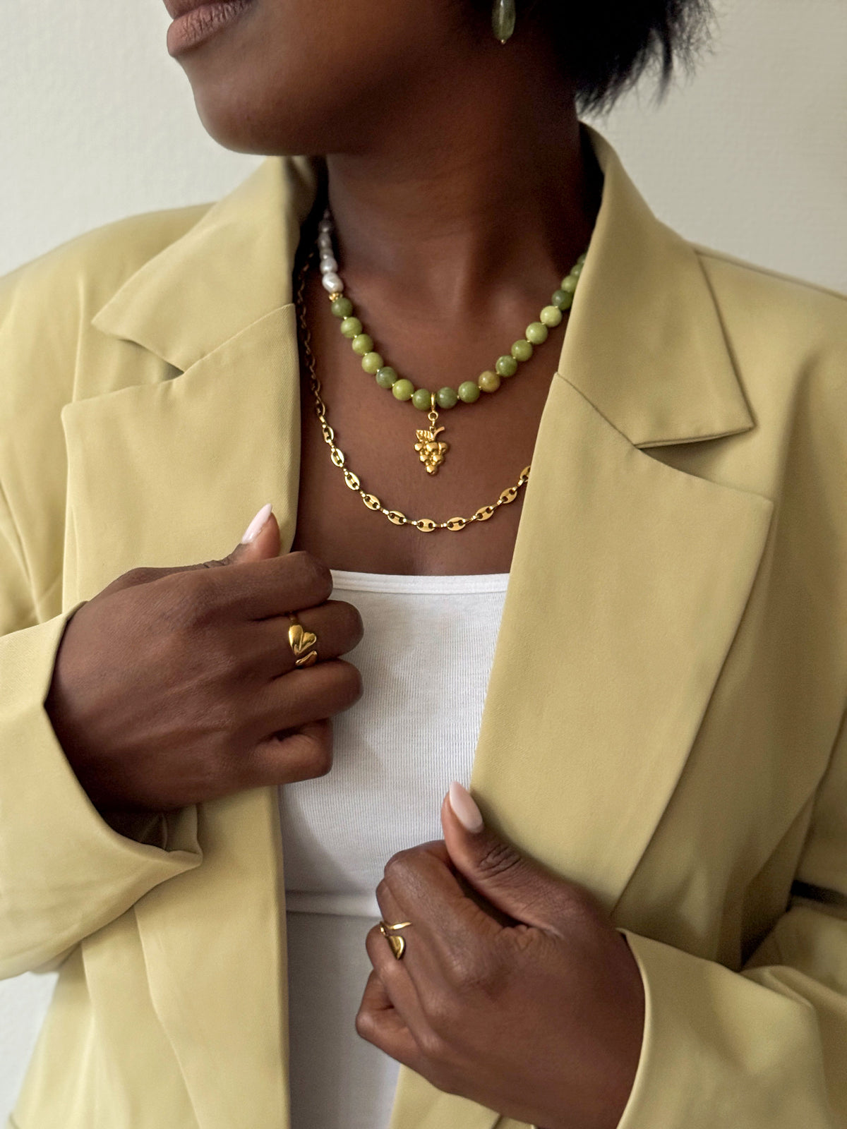 Vrouw draagt een groene kralenketting met gouden druivenbedel, een gouden schakelketting en organische gouden ringen van Don’ aparte.