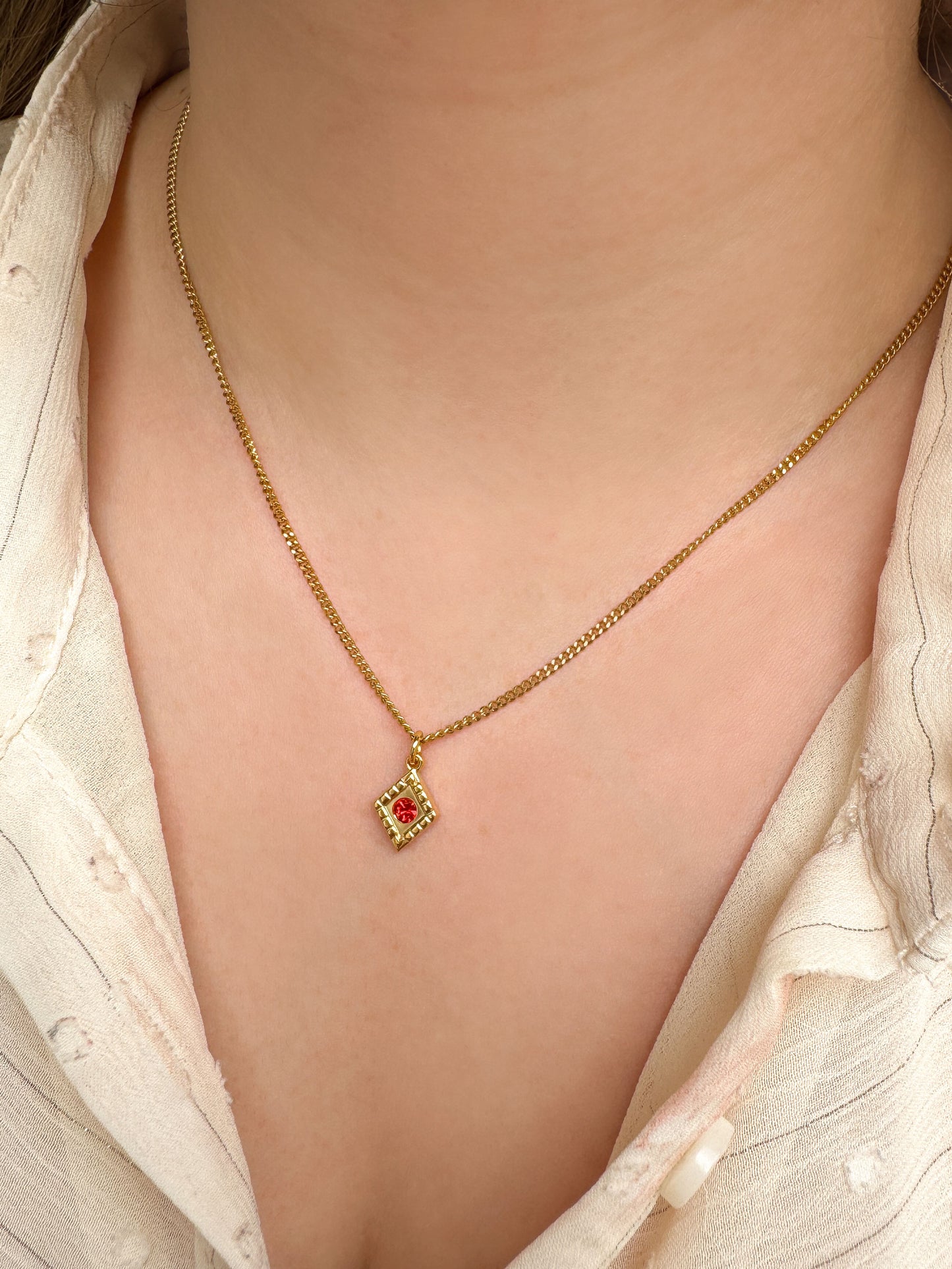 Gouden ketting met ruitjes bedel en rood steentje