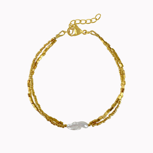 Gouden kralenarmband met fijne kralen en een witte langwerpige parel in het midden.