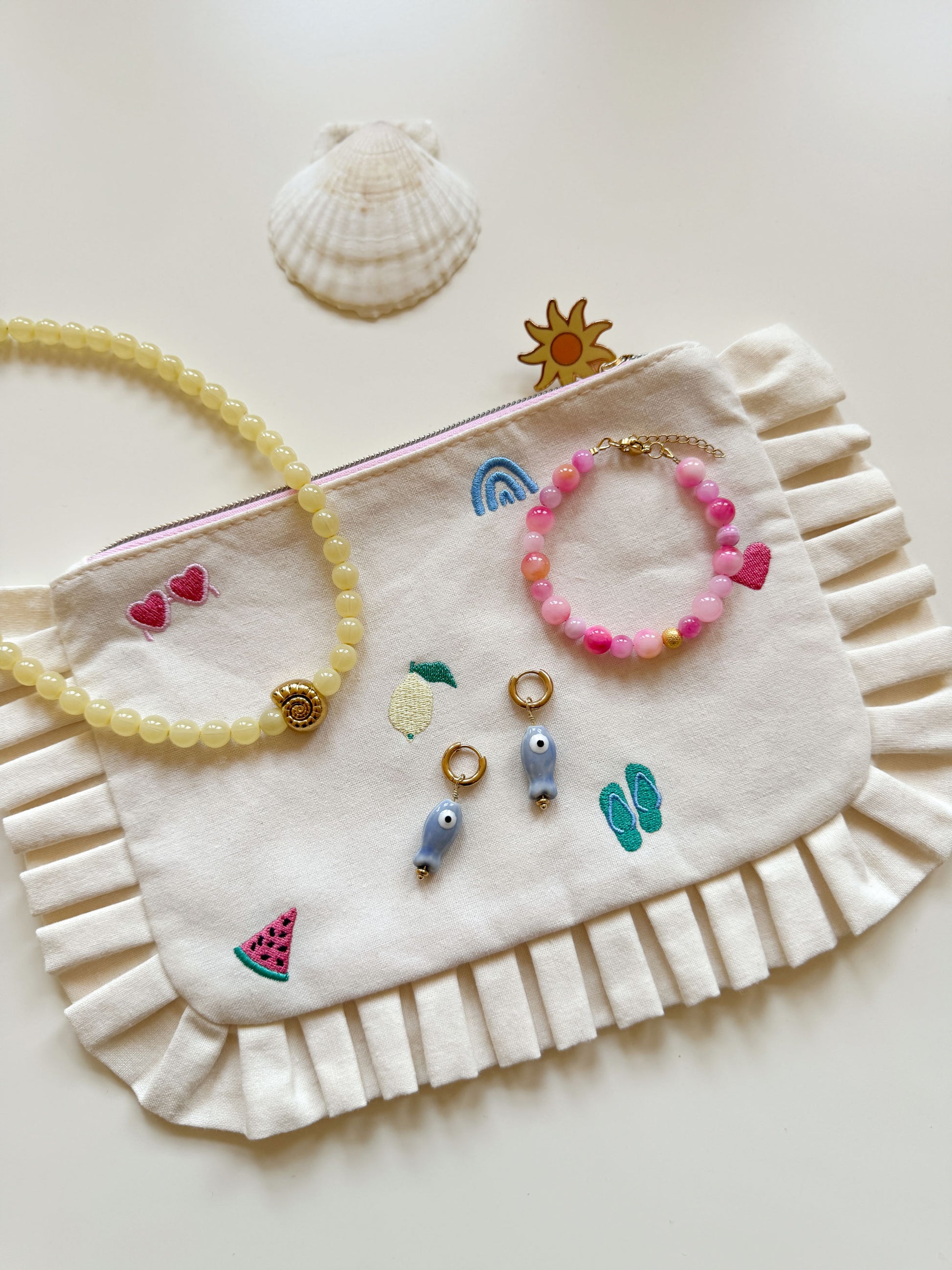 Flatlay met gele ketting, roze armband en oorbellen met visbedel
