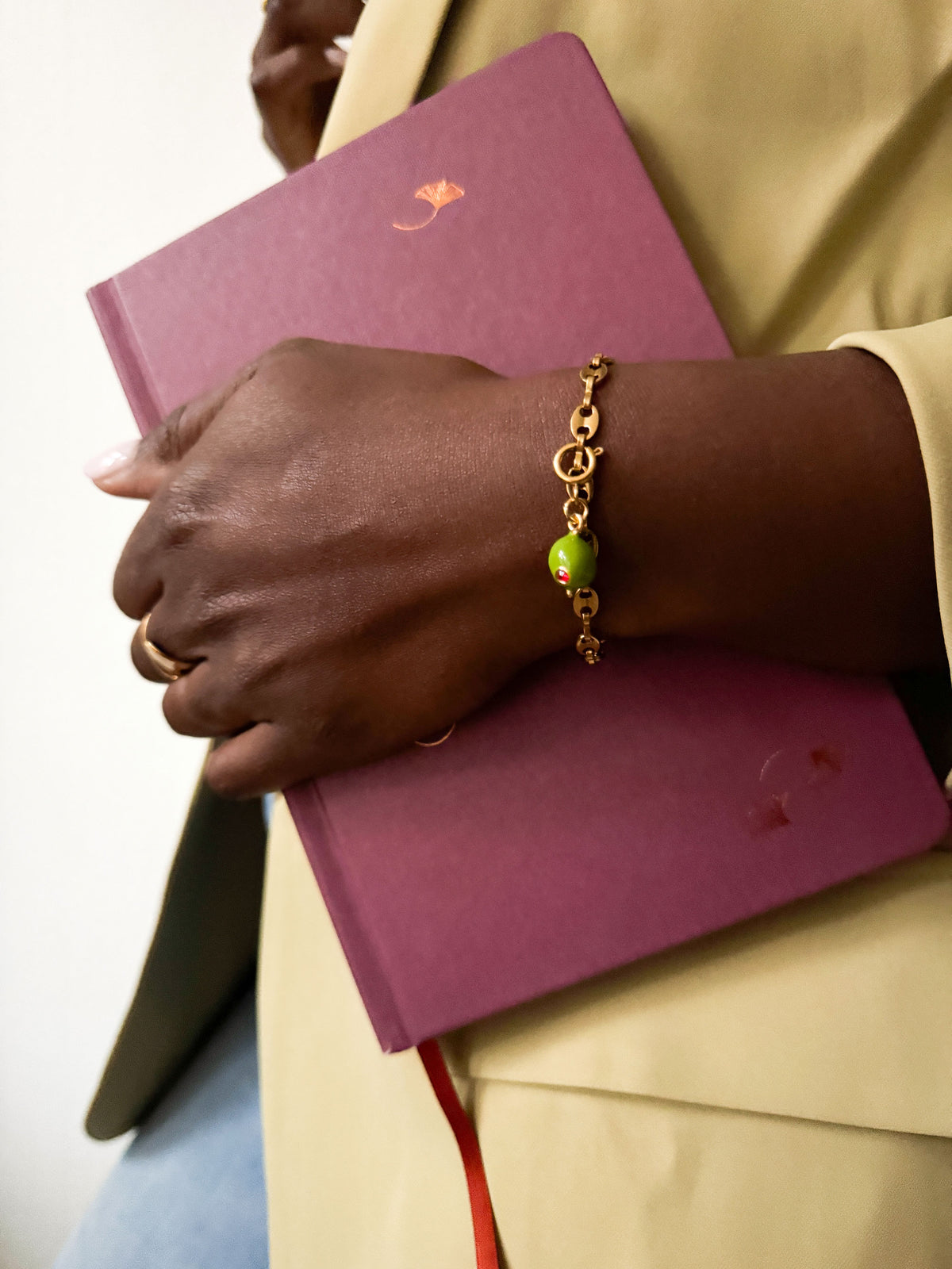 Close-up van een gouden schakelarmband met groene olijfbedel en rood steentje uit de Atelier Colore collectie van Don’ aparte.