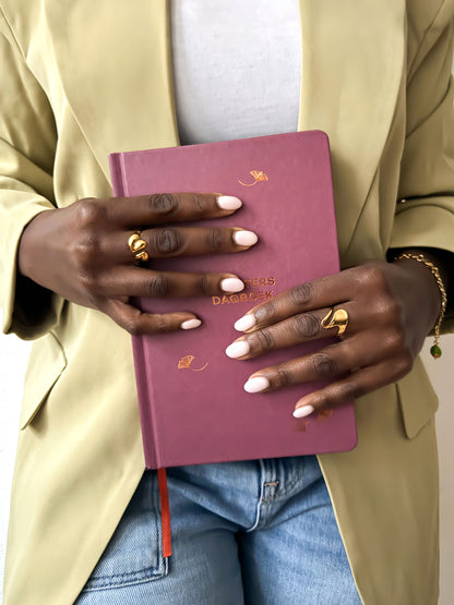 Vrouw draagt gouden statement ringen en een fijne gouden armband met groene bedel uit de Atelier Colore collectie van Don’ aparte, gecombineerd met een lichtgroene blazer.