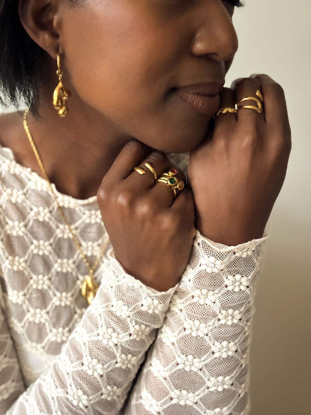 Vrouw draagt gouden statement ringen met groene en rode stenen en organische gouden ringen van Don’ aparte, gecombineerd met een witte kanten top.