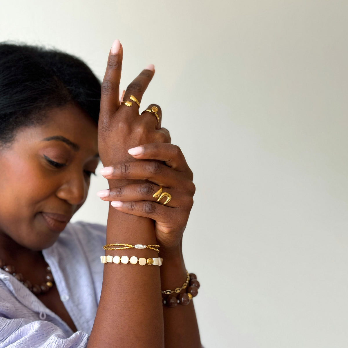 Vrouw met gouden organische ringen, een crème kralenarmband, een fijne gouden armband met parel en een bruine kralenarmband van Don’ aparte.
